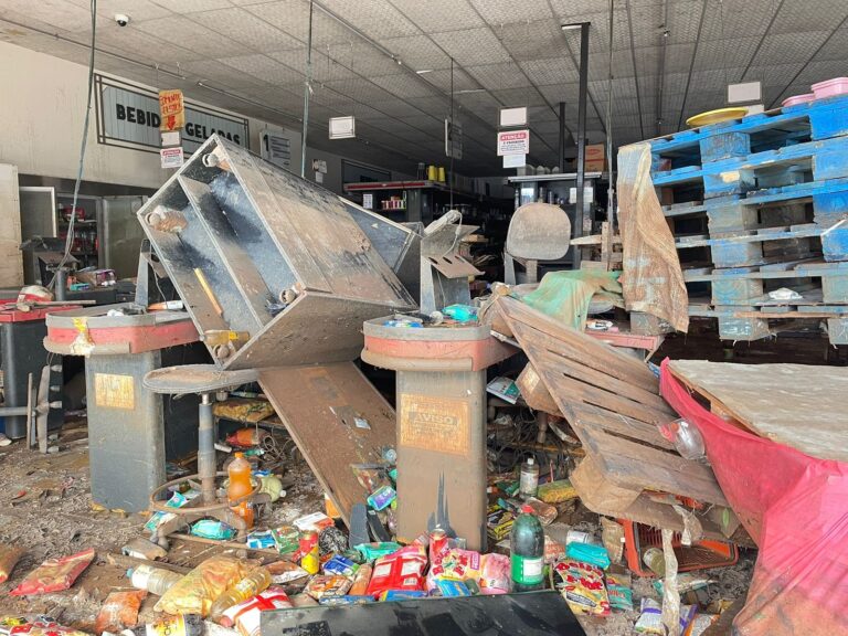 Enchente em Canoas: “O cheiro está insuportável” relata moradora vizinha a supermercado. Pela porta é possível ver o cenário.