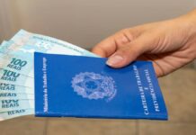Mão de trabalhador segurando carteira de trabalho e dinheiro de crédito consignado CLT