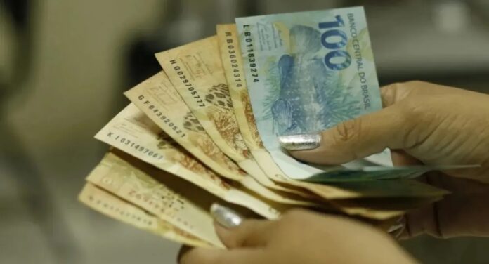 Mãos de mulher segurando diversas notas de reais sacando o salário mínimo