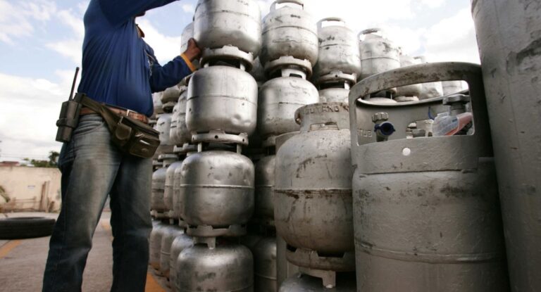 Imagem mostra um homem pegando um botijão de gás; Auxílio do governo pago em vale, deixará de existir