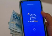 Foto mostra uma pessoa segurando um celular com o aplicativo do Caixa Tem e notas de dinheiro