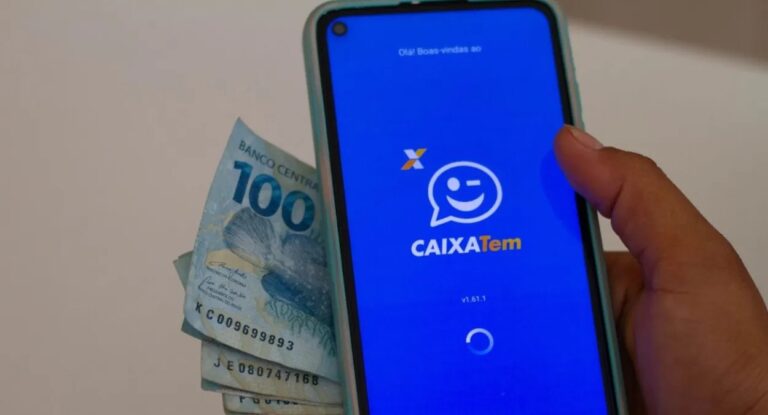 Foto mostra uma pessoa segurando um celular com o aplicativo do Caixa Tem e notas de dinheiro