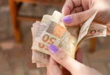 Foto mostra pessoa contando cédulas de dinheiro de auxílio do caixa tem