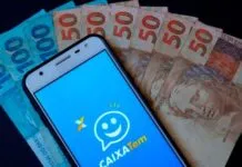 Celular com o aplicativo do Caixa Tem com cédulas ao fundo