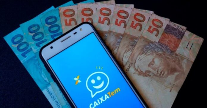 Celular com o aplicativo do Caixa Tem com cédulas ao fundo