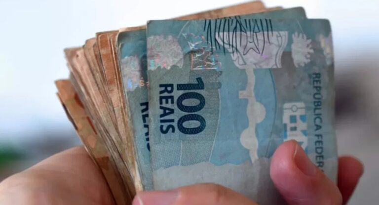 Imagem de mãos segurando cédulas de dinheiro com valores de R$50 e R$100 reais