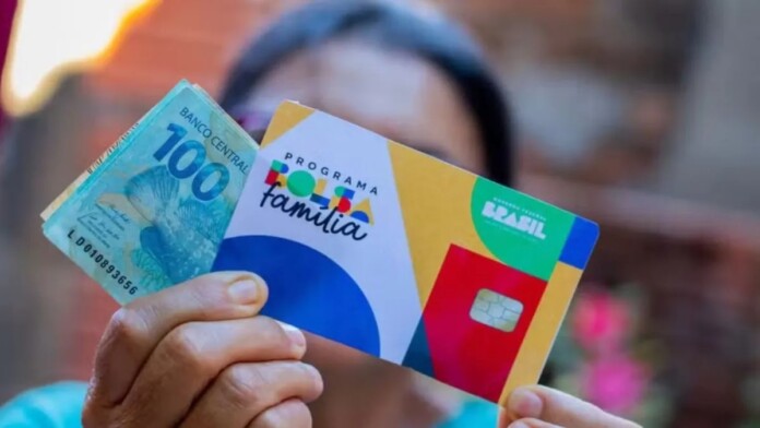 foto mostra beneficiário segurando cartão do bolsa família com notas de dinheiro do auxílio