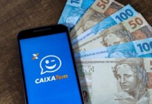 Celular com o app do Caixa Tem aberto e cédulas de dinheiro ao fundo