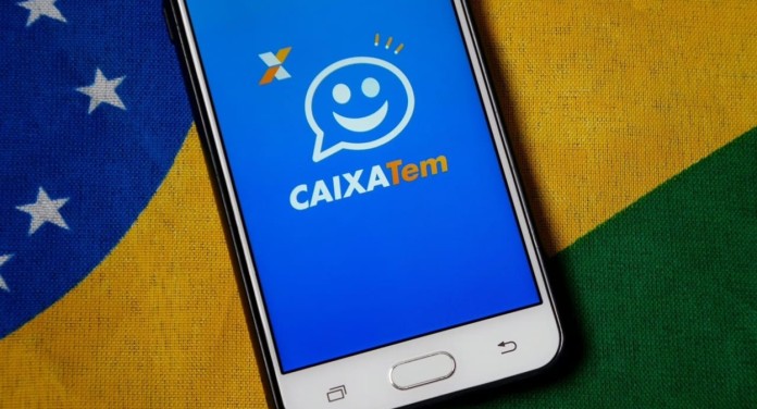 Foto mostra o aplicativo do Caixa Tem em um celular com a bandeira do Brasil de fundo.